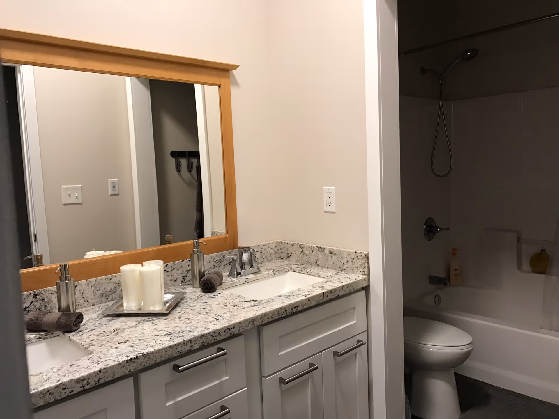 Bathroom with a granite double-sink vanity and large mirror, and a toilet with a shower-tub alcove.
