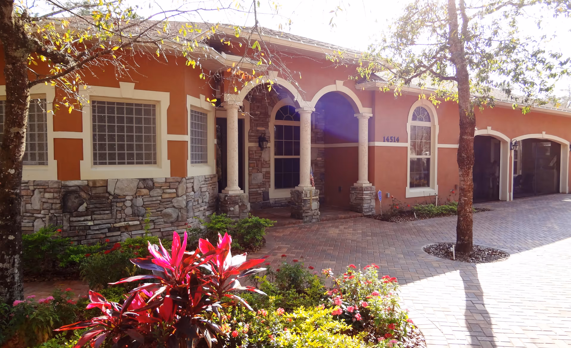 Front exterior of a single-story residence with an arched columned entry, stone accents, two-car garage, and landscaped driveway.