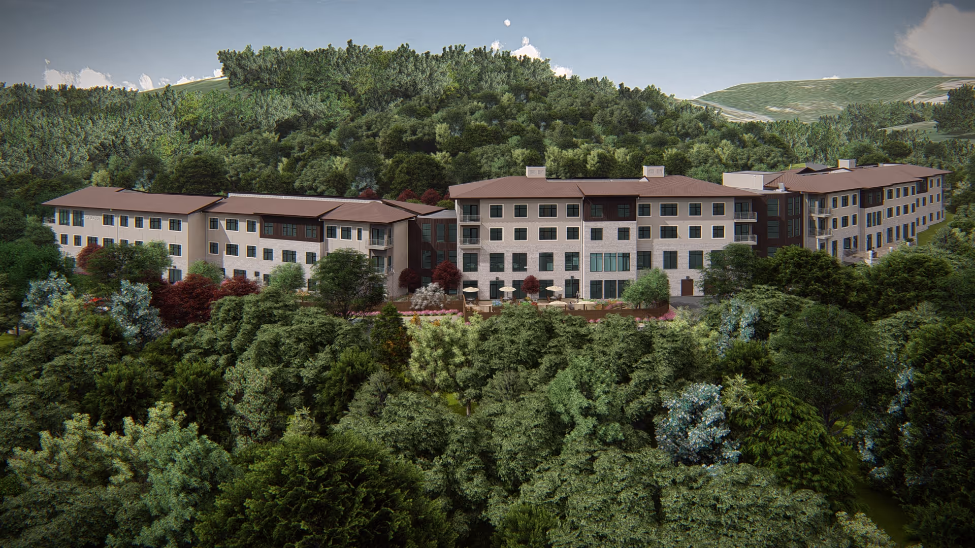 A large multi-story senior living facility building surrounded by dense green trees and hills in the background under a partly cloudy sky.