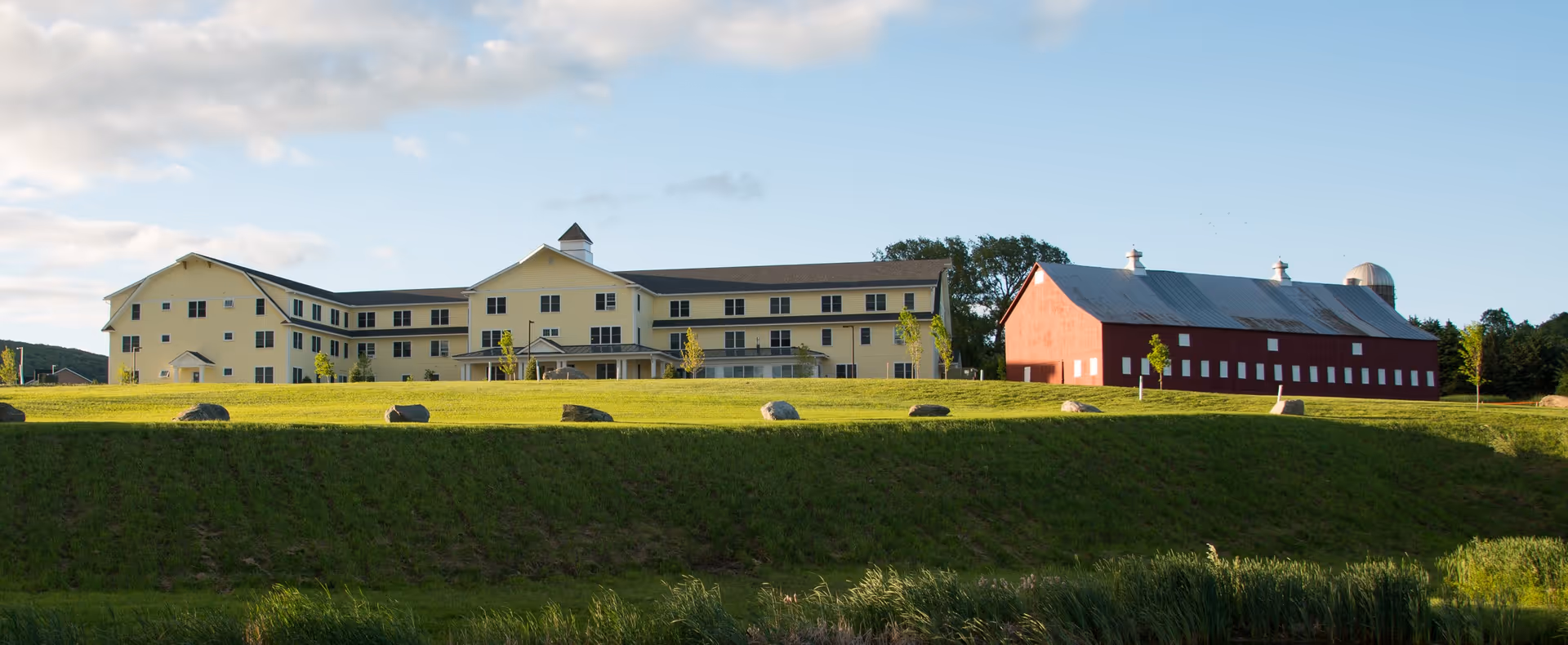 Exterior view of Homestead Senior Living campus with beige buildings and a red barn.