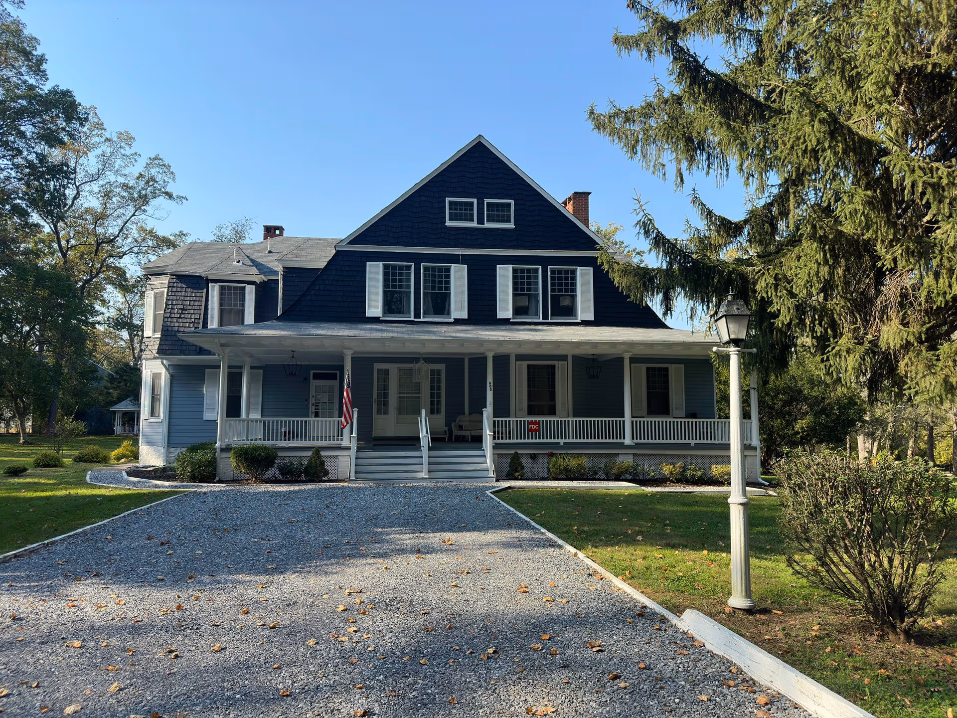 Blue, two-story house-style senior living facility with a front porch and gravel driveway.