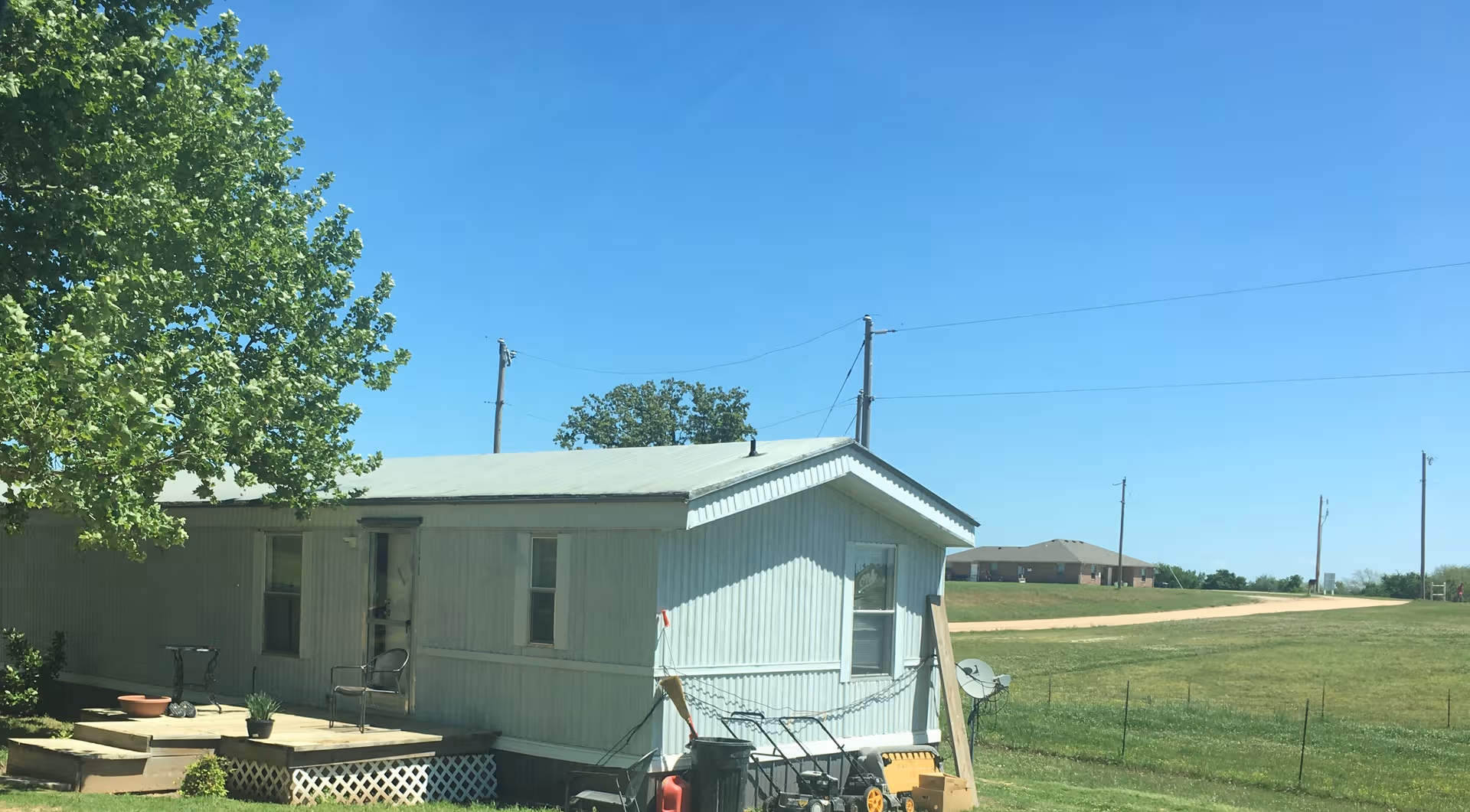 Front exterior of a small light-blue modular home with a porch and tree.