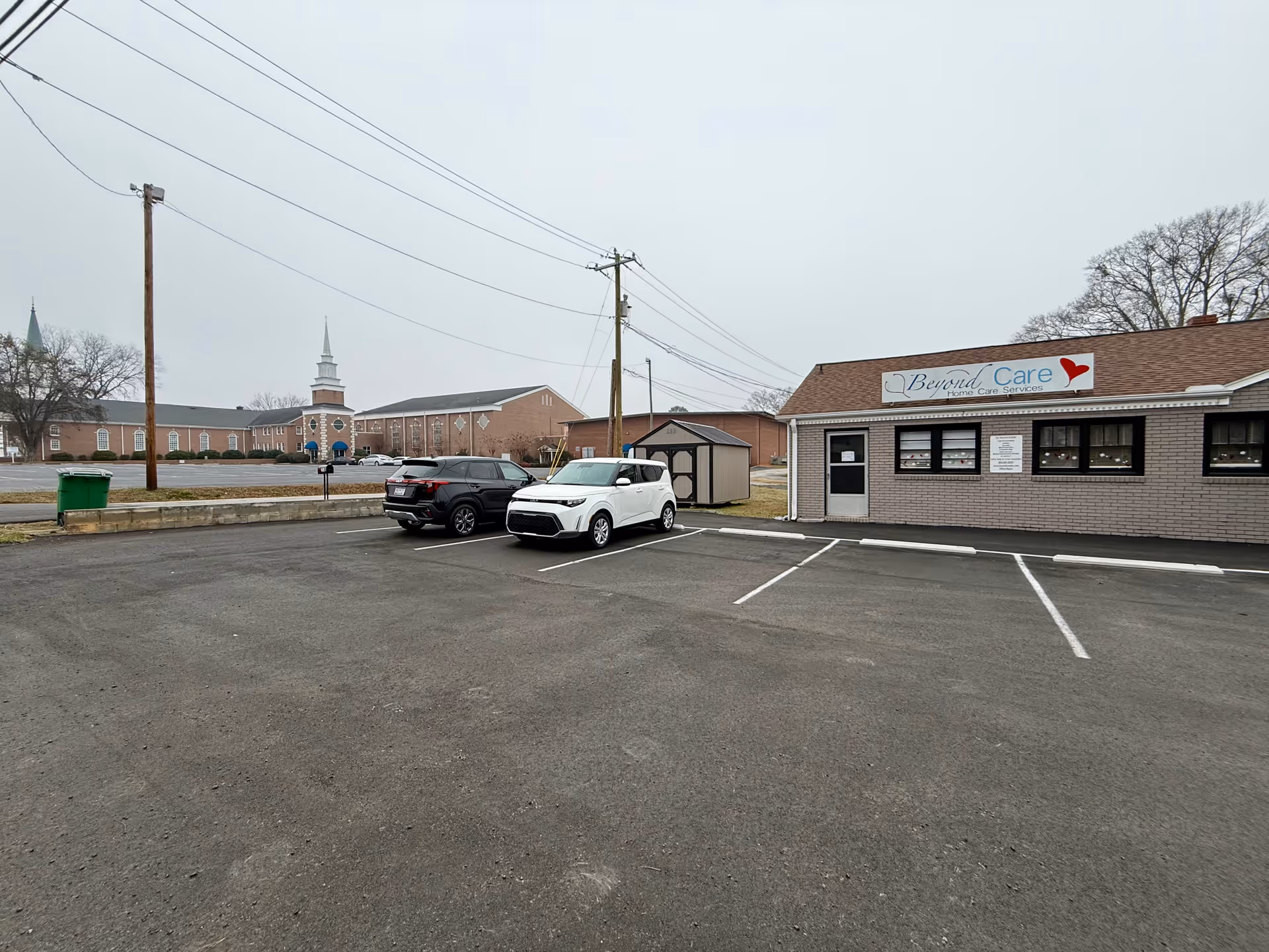 Parking lot in front of Beyond Care facility; brick building with sign.