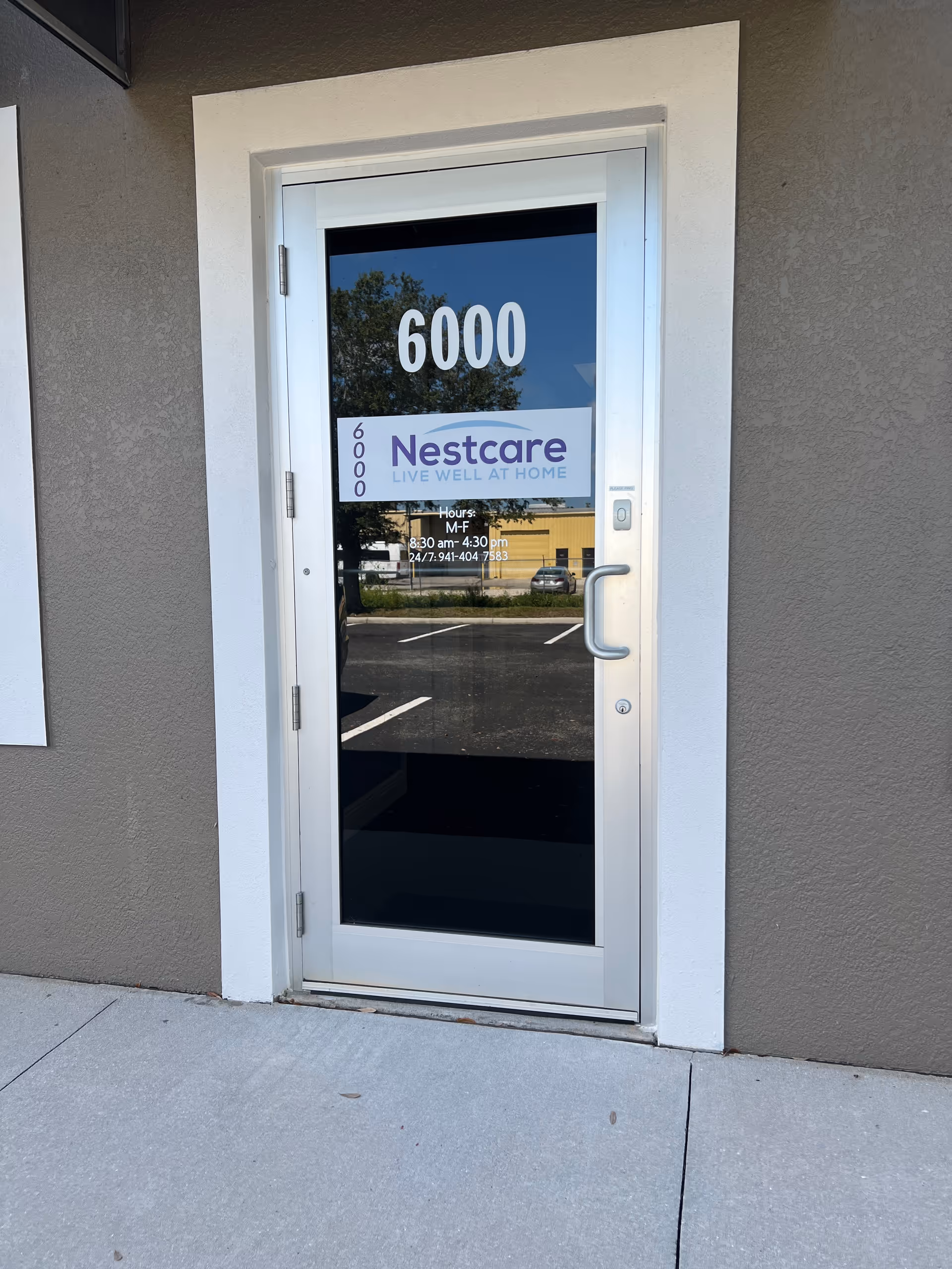 Glass entry door with Nestcare sign, exterior building facade and reflection of street.