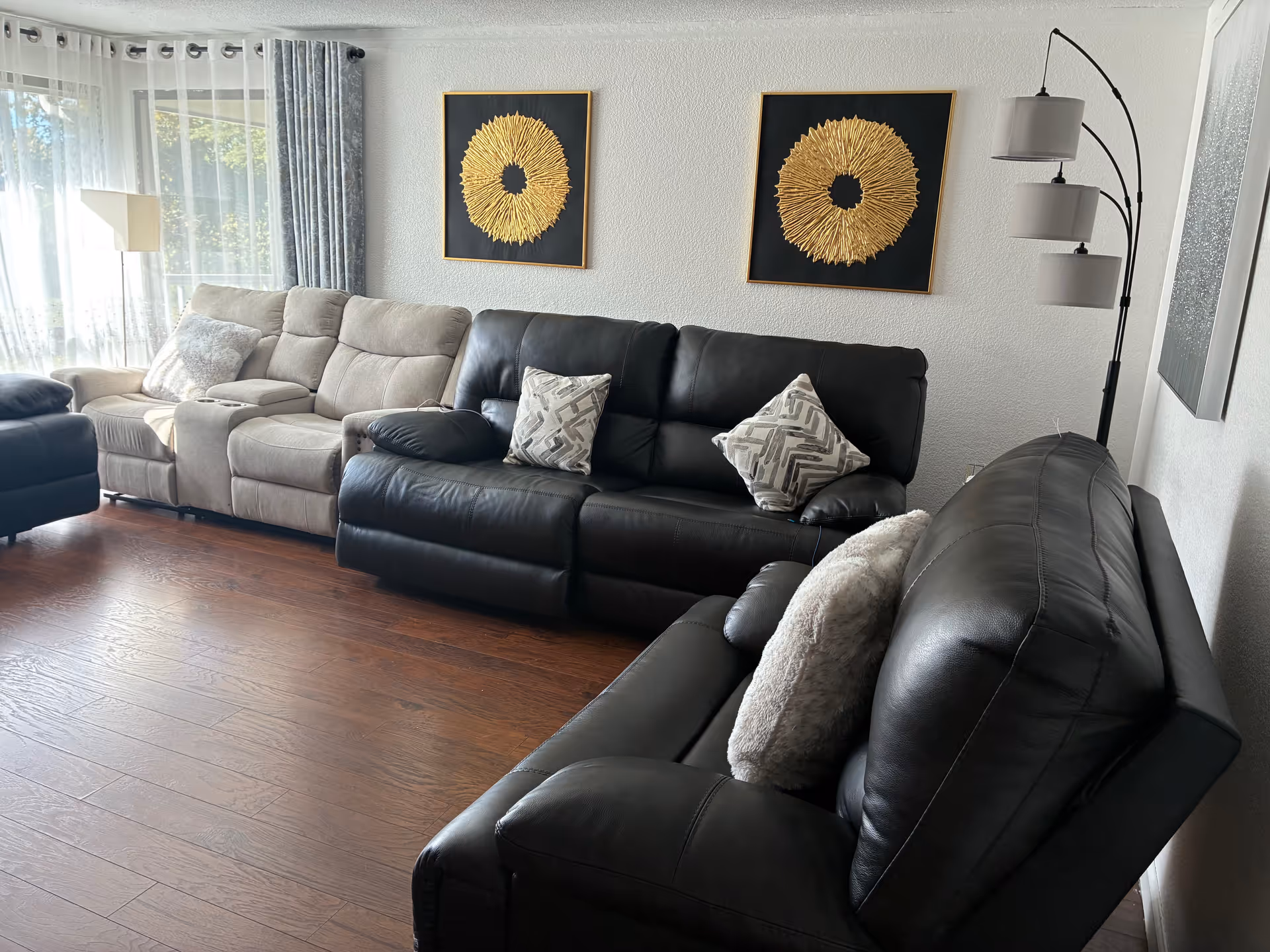 Cozy living room with beige and black leather sofas, wall art, and a floor lamp.