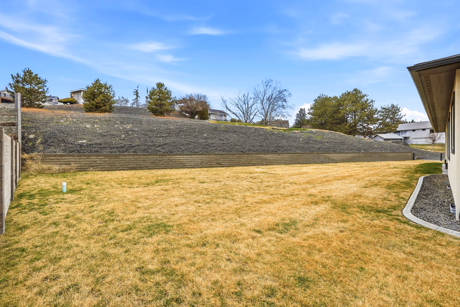 Outdoor grassy yard with a stone retaining wall on a slope behind the building.
