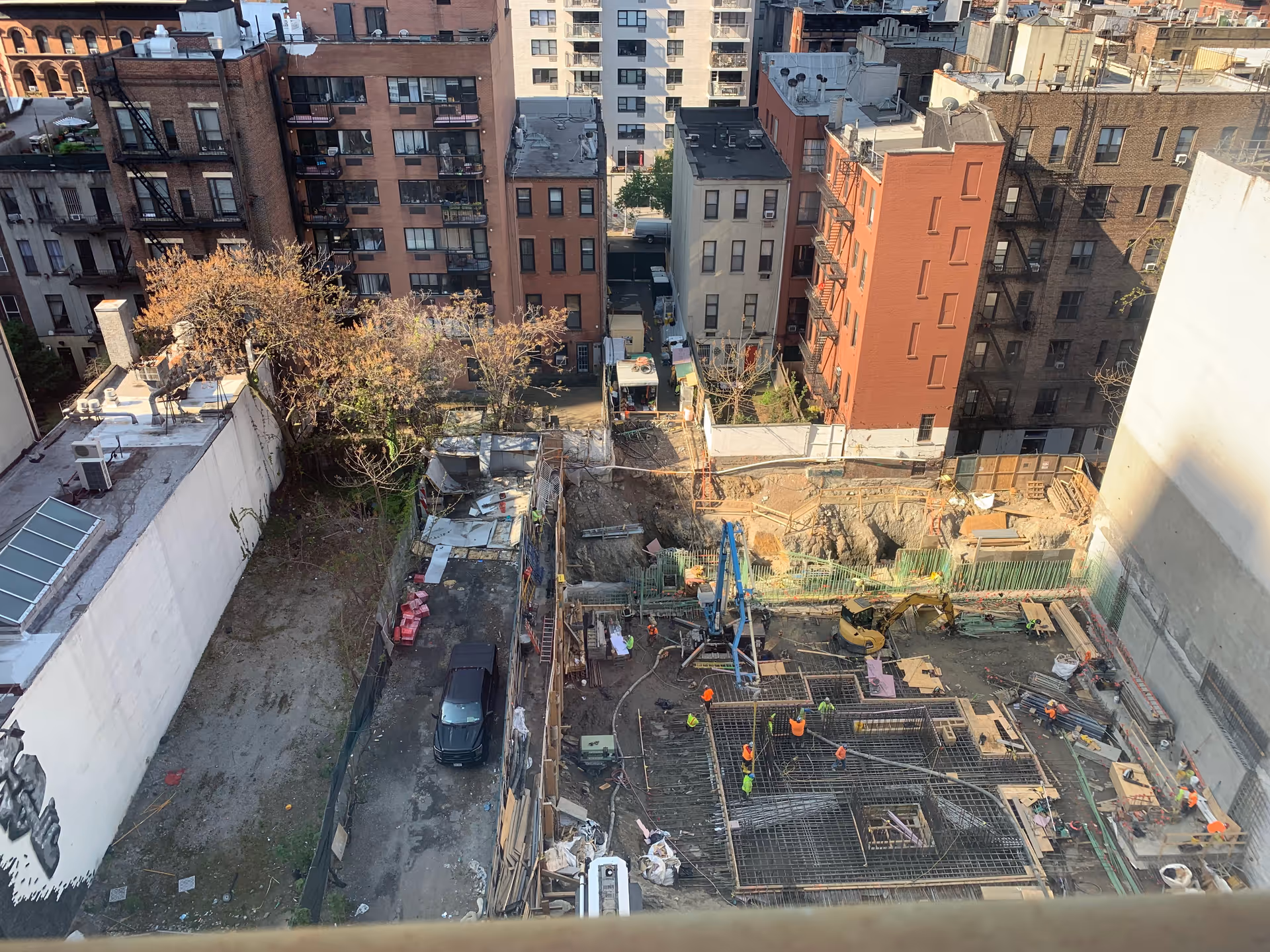 Urban construction site with workers and heavy equipment amid mid-rise buildings.