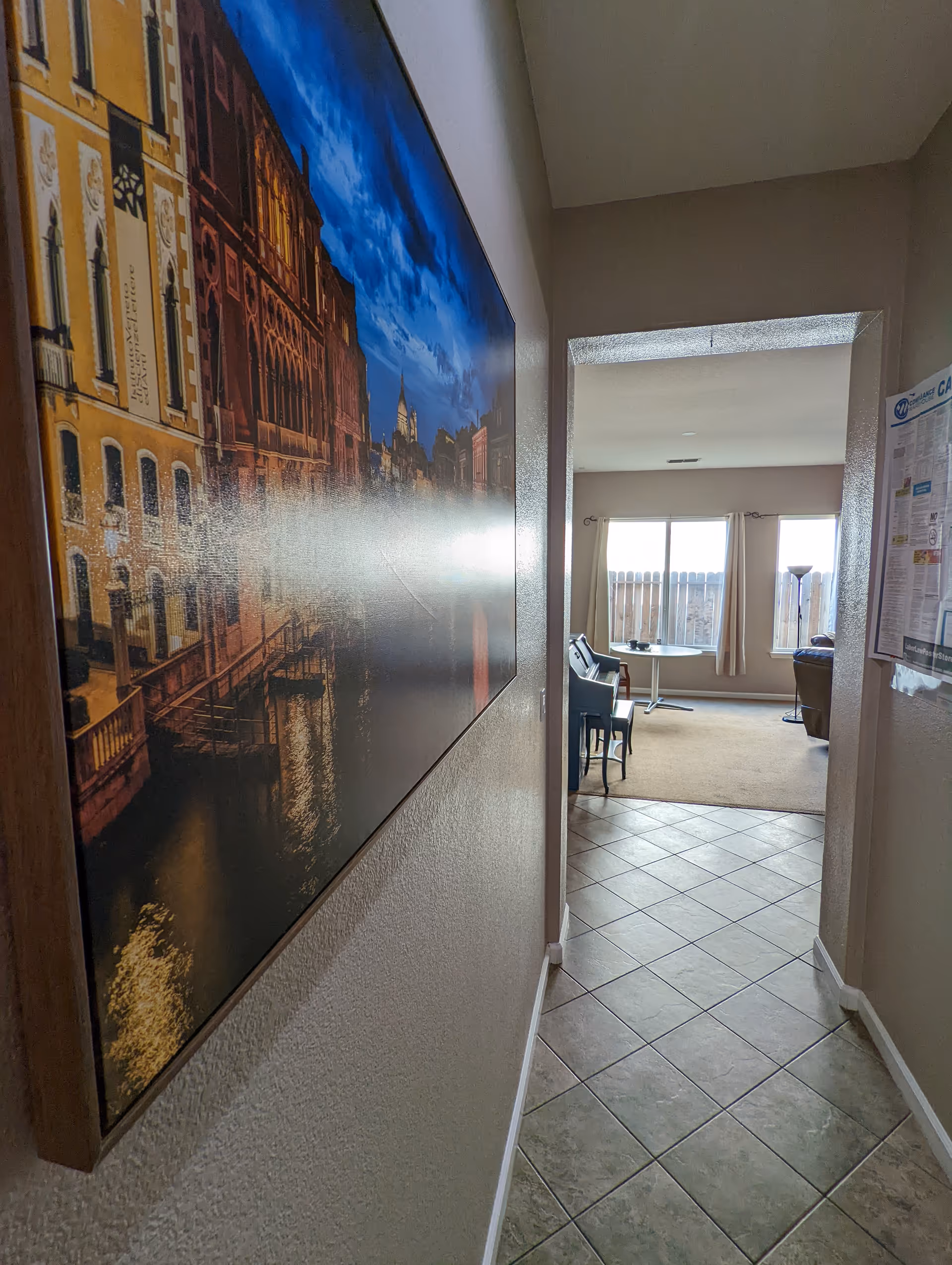 Narrow hallway with framed cityscape leads to a bright living area and windows.