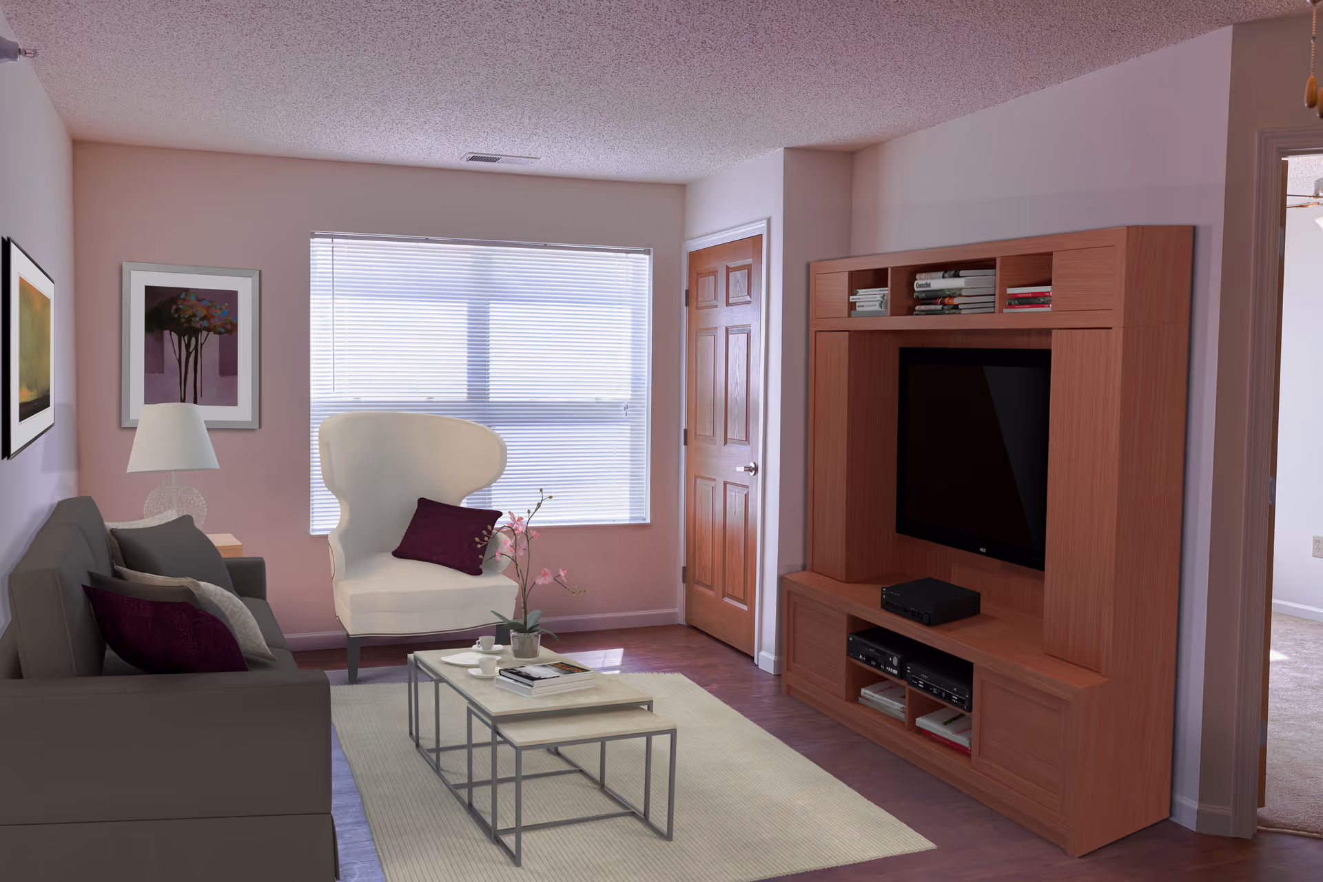 A cozy living room with a gray sofa adorned with purple and gray pillows, a white armchair with a purple pillow, a coffee table with books and a flower vase, a wooden entertainment center with a TV and shelves filled with books, and a window with blinds letting in natural light.