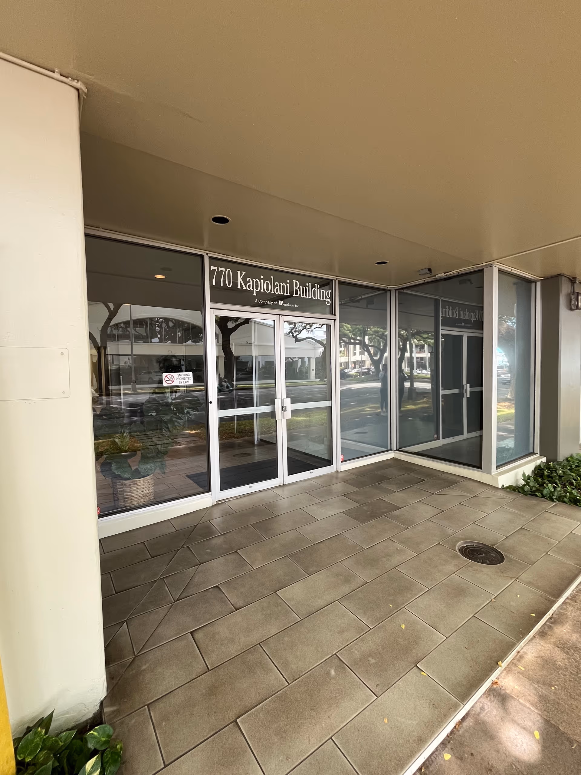 Exterior entrance to 770 Kapiolani Building with glass doors and tiled walkway.