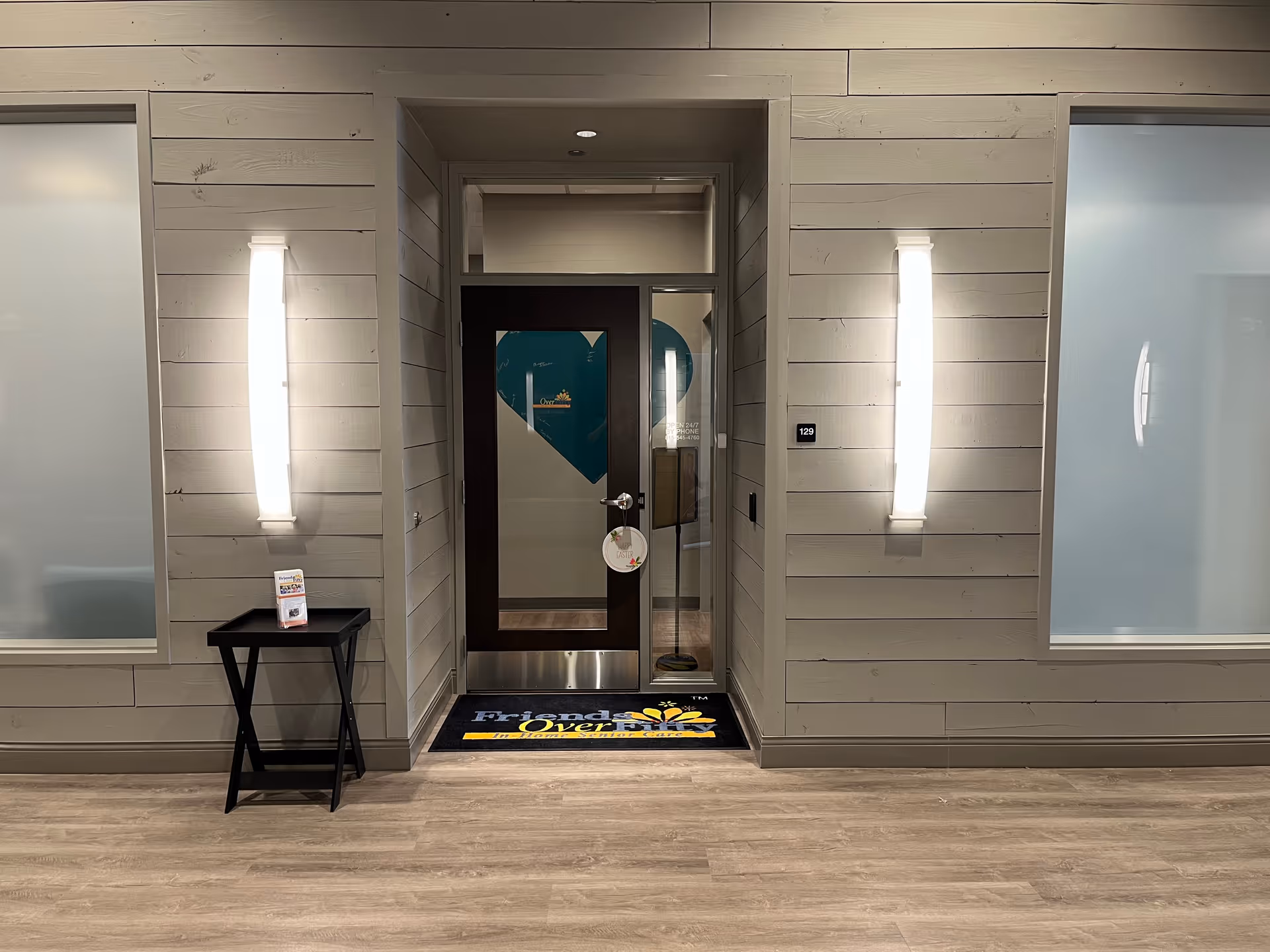 Interior hallway entrance of Friends Over Fifty Senior Care, with door, side lights, and welcome mat.