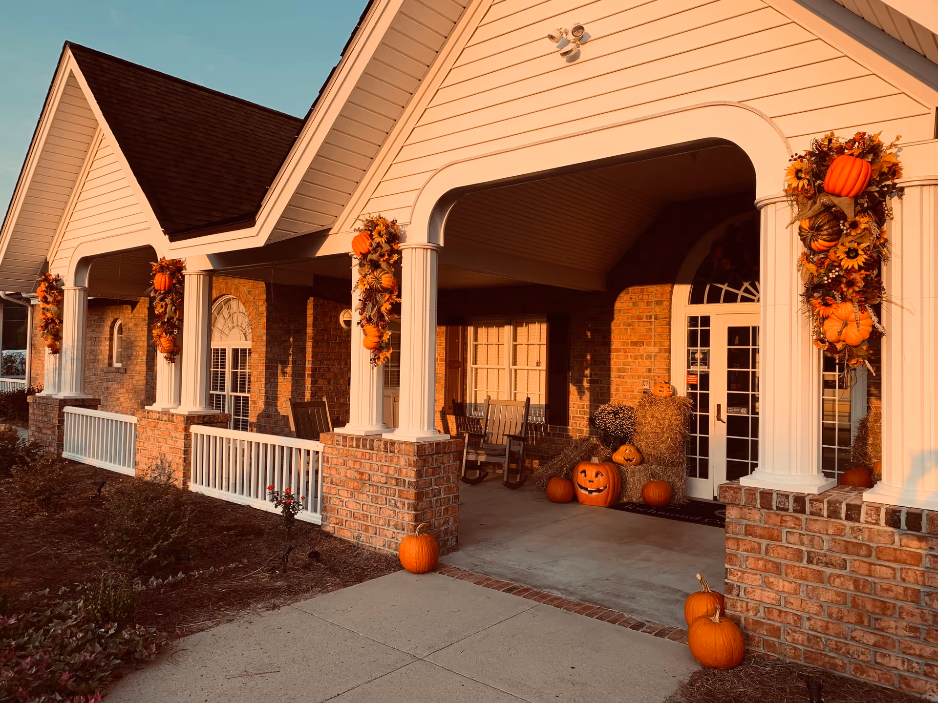 Front porch of a brick building decorated with pumpkins and autumn garlands.