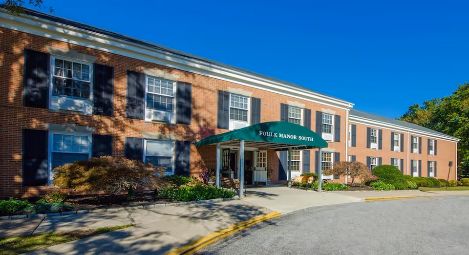 Brick senior living facility exterior with a green entrance canopy and manicured landscaping.