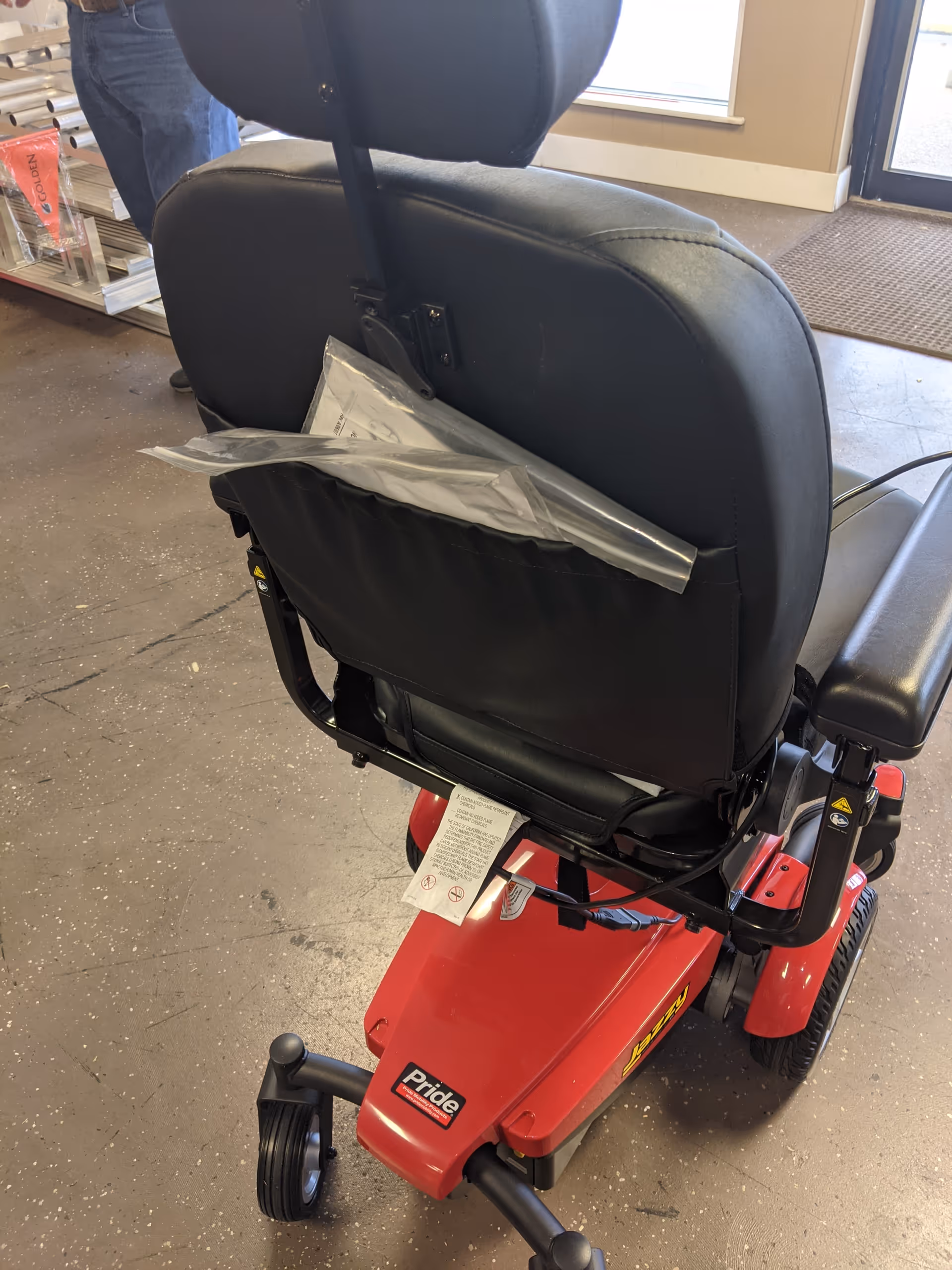 Red mobility scooter on display indoors near doorway and shelves.