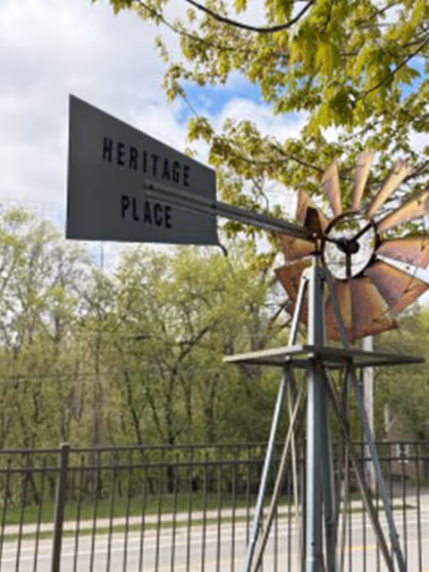 Exterior Heritage Place sign with a windmill sculpture and green trees in the background.