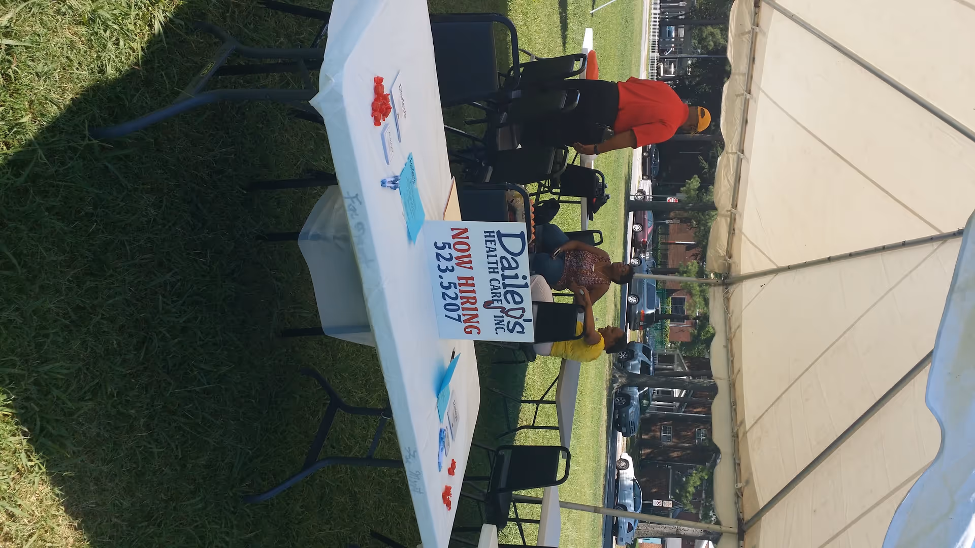 Outdoor tent setup with tables, people, and a Now Hiring sign for Dailey's Health Care.