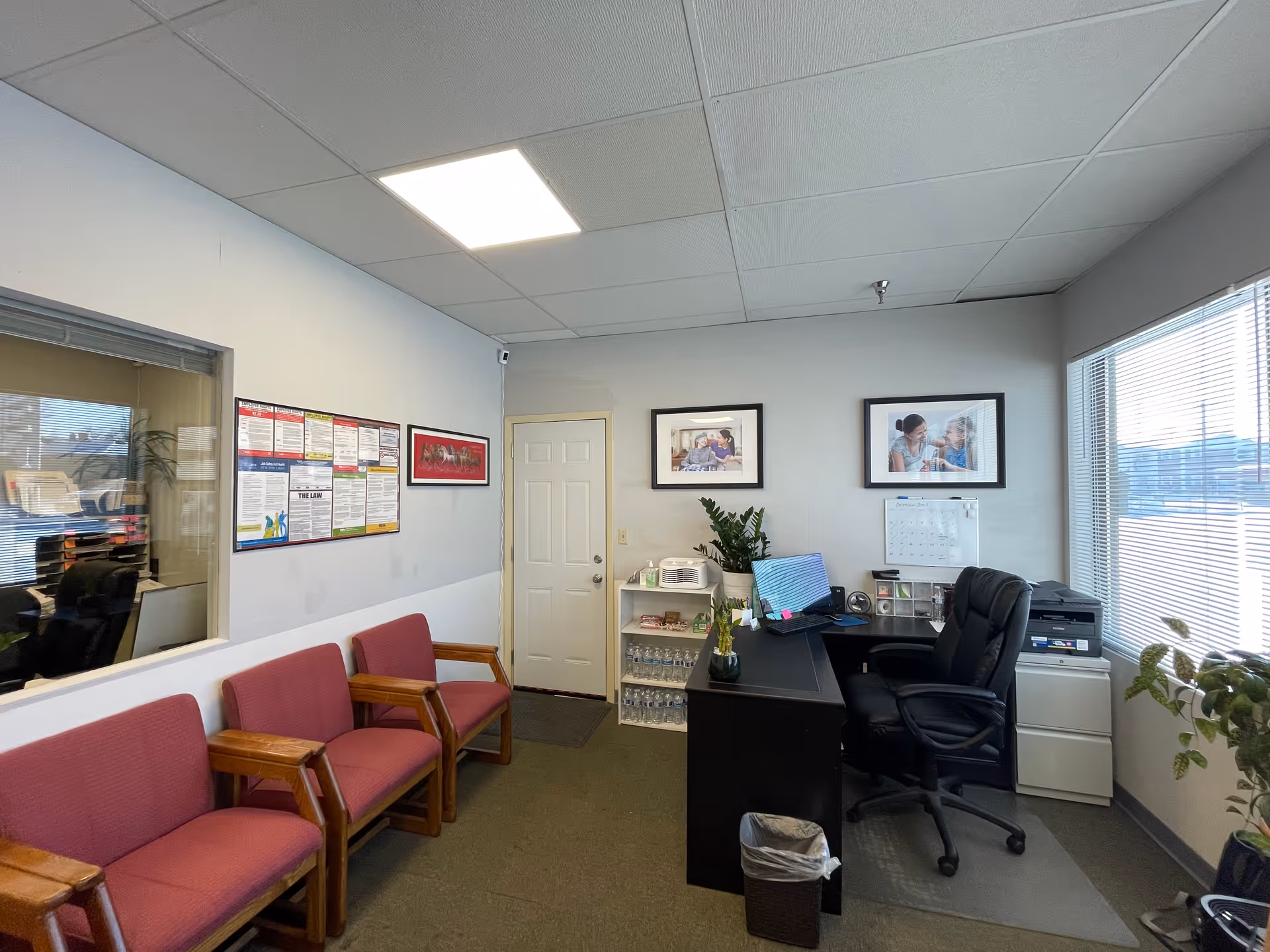 Office reception area with pink chairs, front desk, printer, and framed photos inside facility.