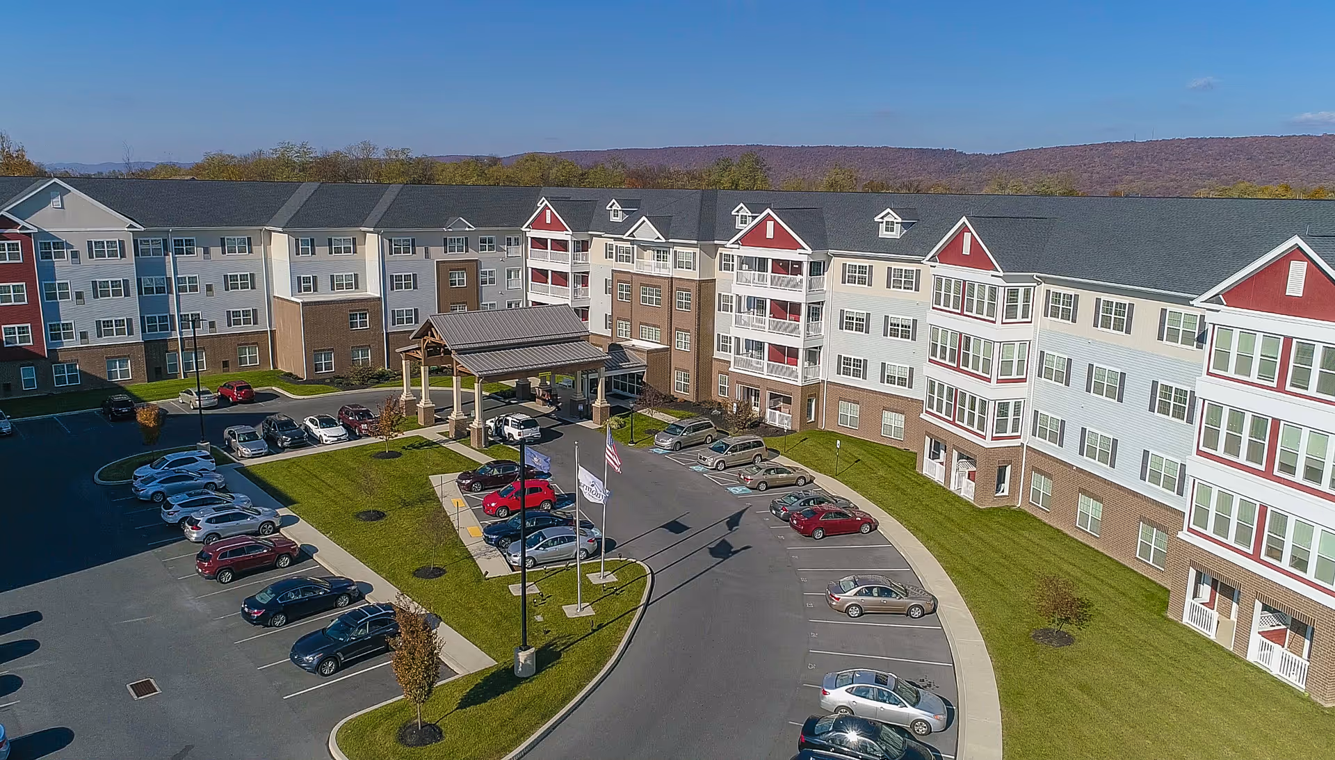 Aerial view of Harmony at West Shore senior living facility, featuring a parking lot and landscaped entrance.