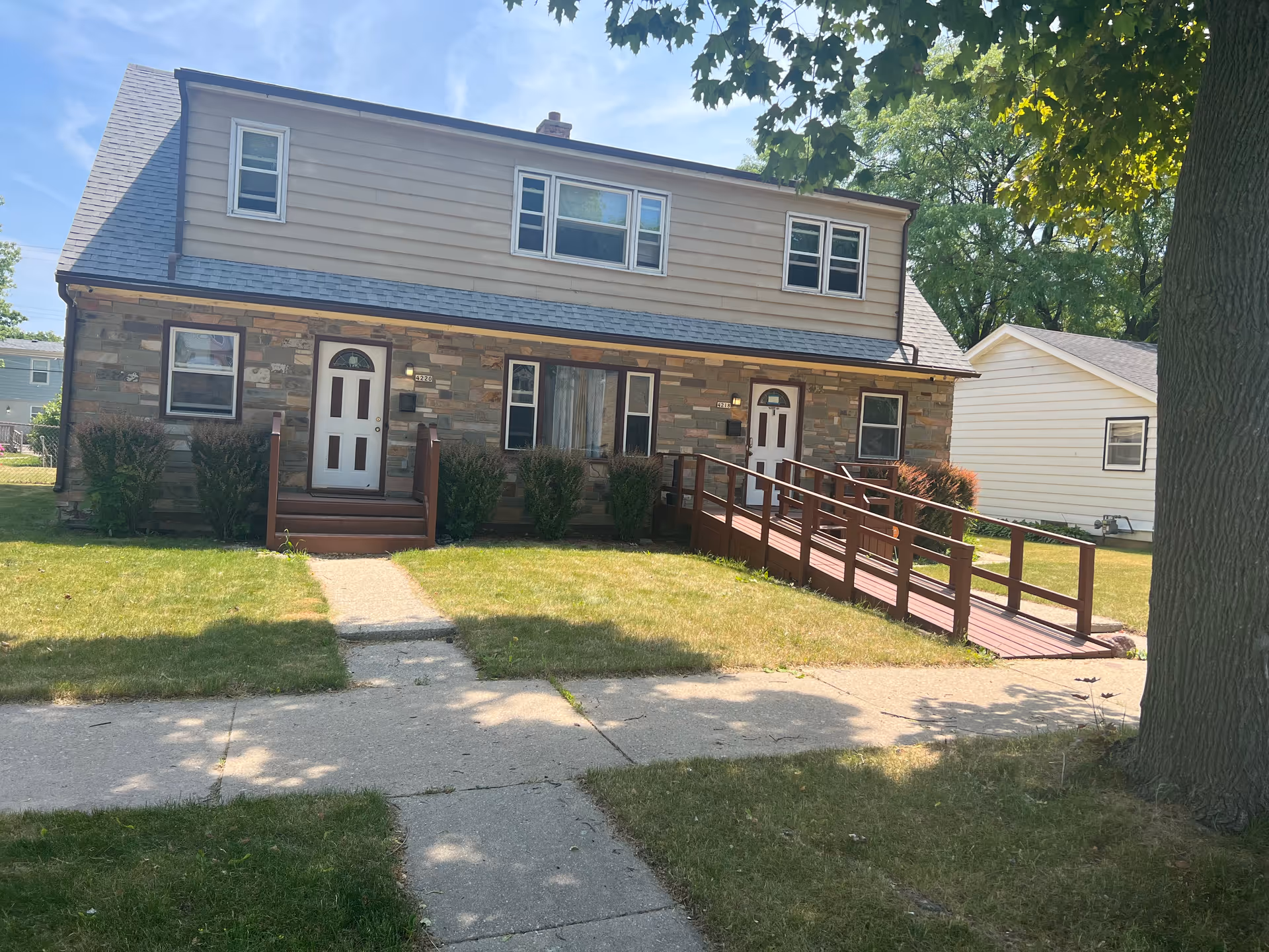 Two-story adult family home with stone facade, two front doors, and a wooden ramp.