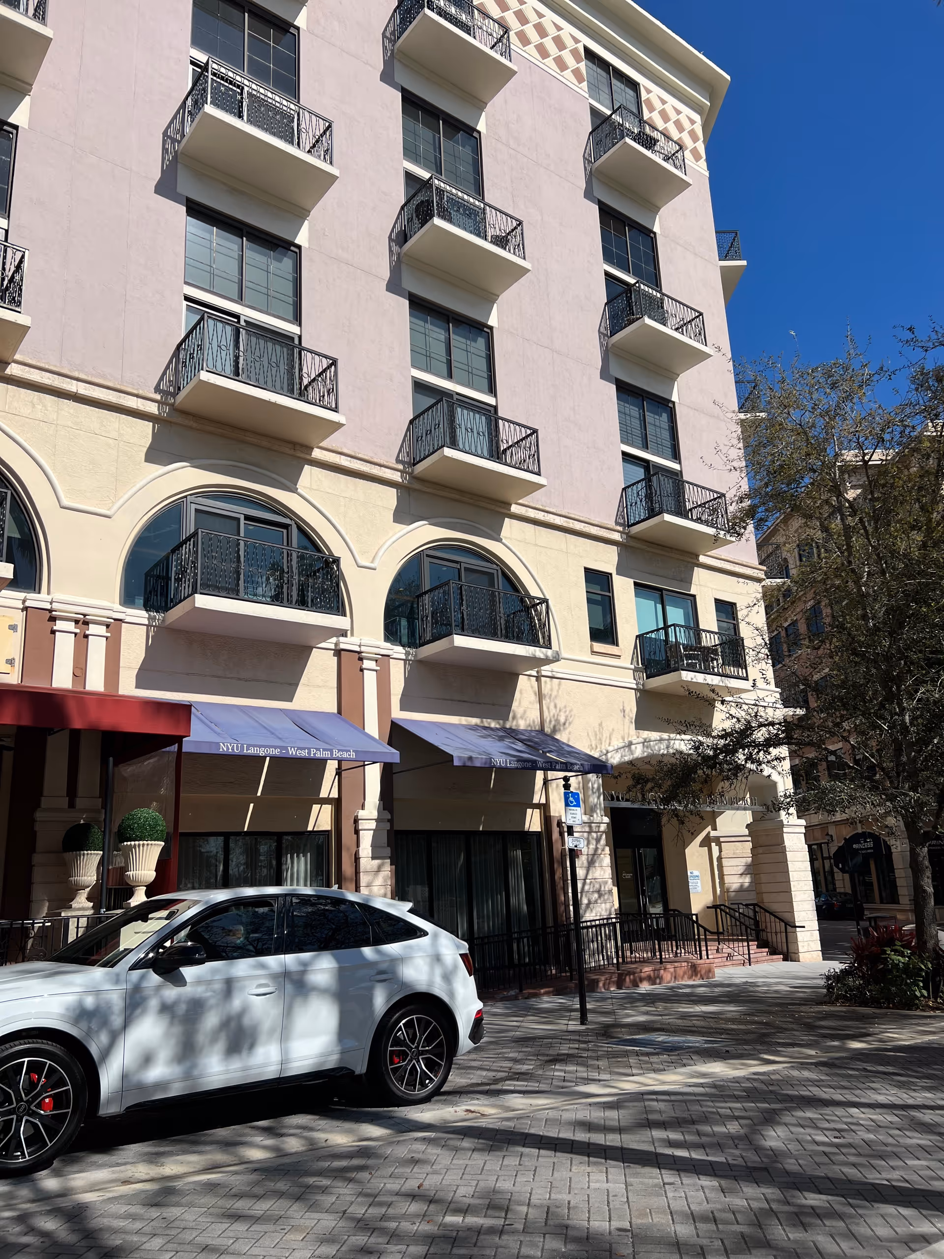 Multistory pink building with balconies and awnings, a white car parked along the street in front