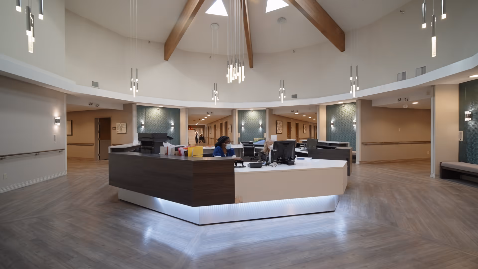 Circular reception desk in a spacious modern lobby with pendant lights and wood beams overhead.