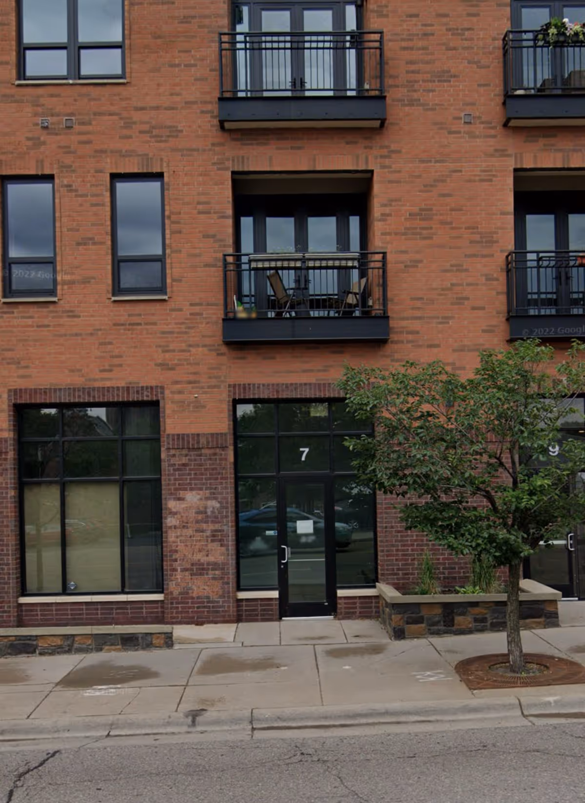 Brick apartment building exterior with balconies and a street-level entrance marked 7.
