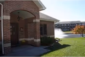 Brick entry arch and front door with fountain and manicured lawn visible.