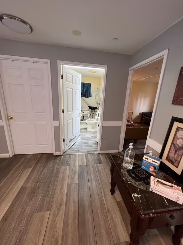 Interior hallway with an open bathroom door revealing toilet and shower in a senior facility.