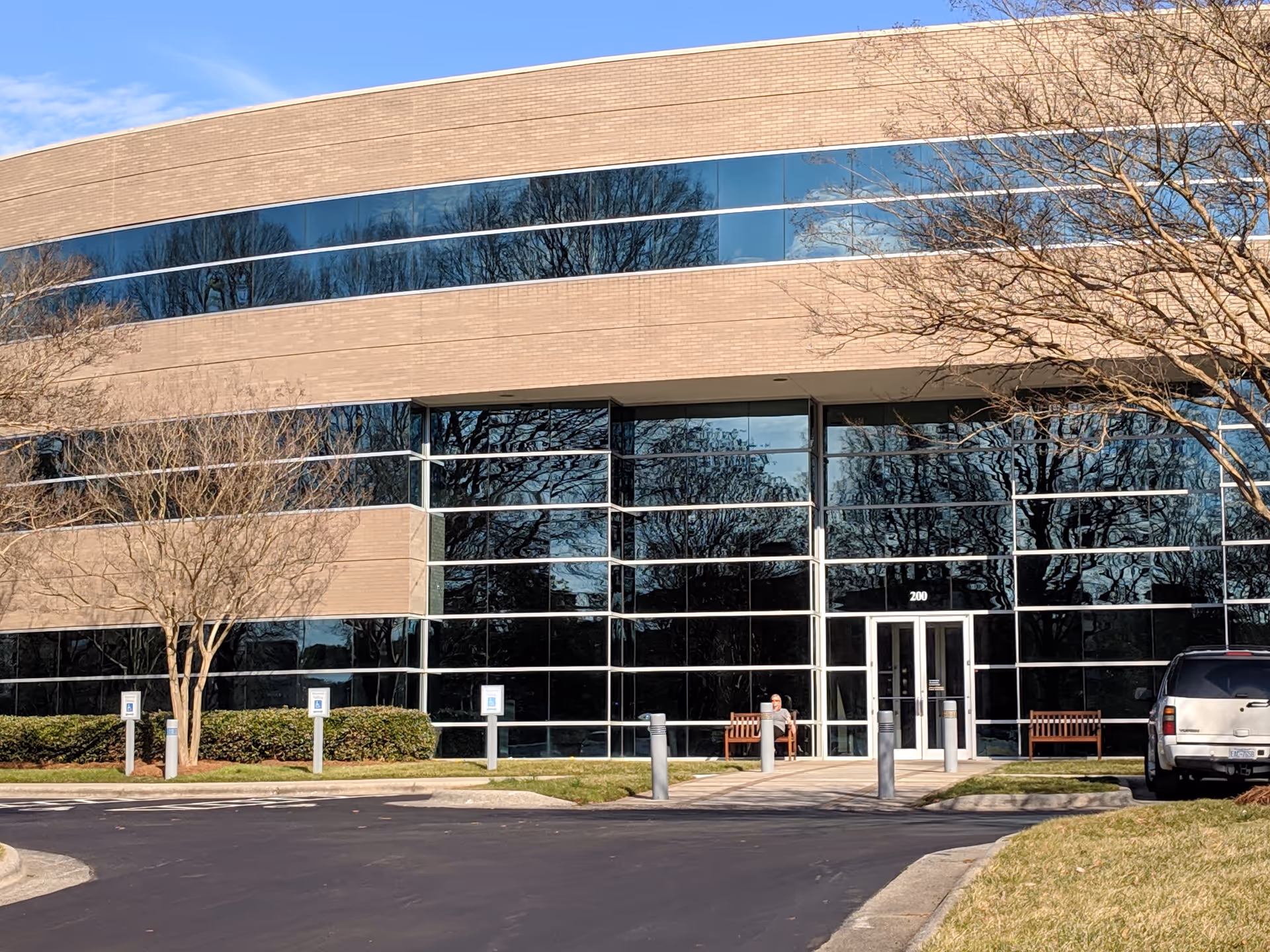 Modern brick-and-glass office building with large windows, trees, and a person near entrance.