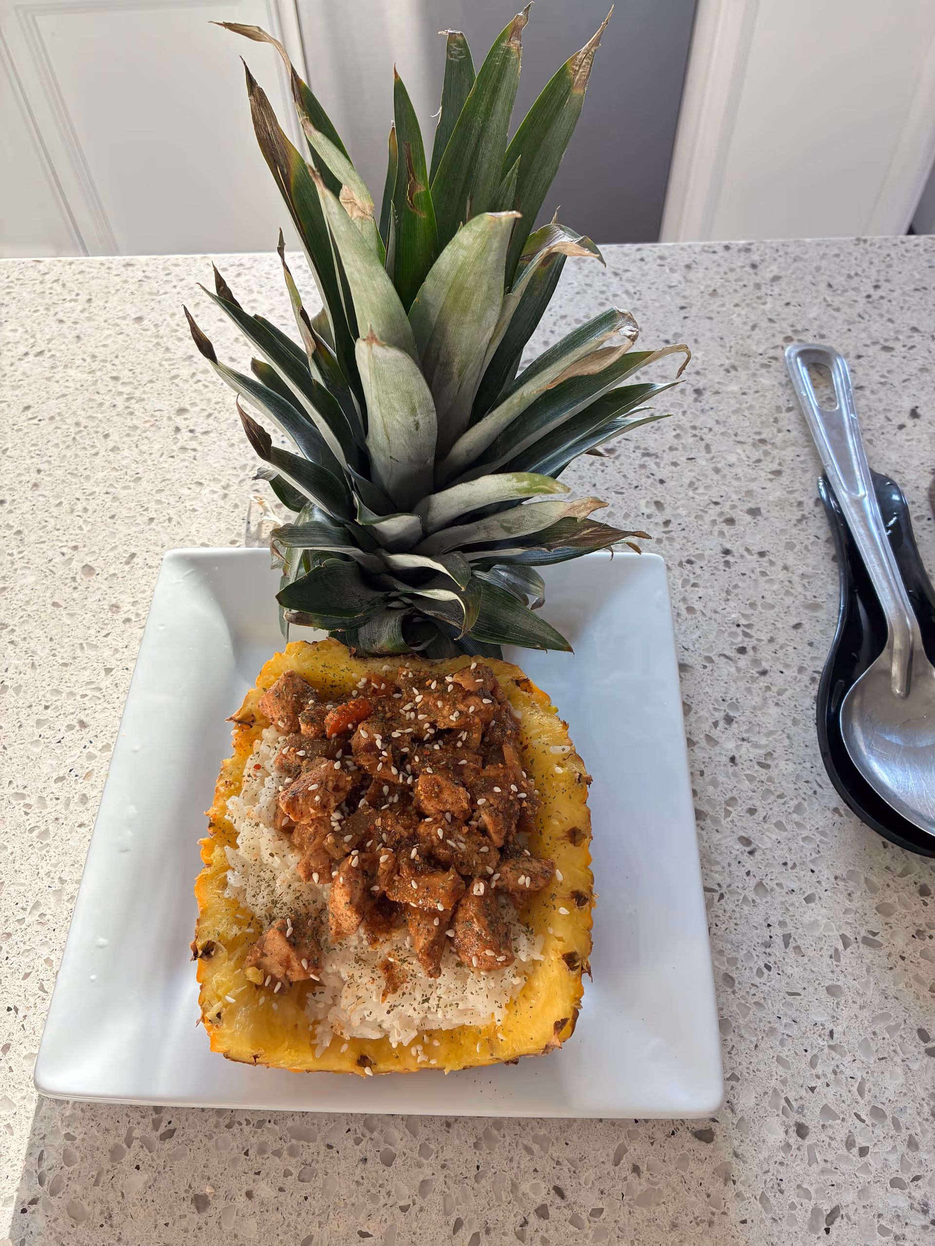 A plated pineapple dessert topped with sesame seeds on a speckled kitchen counter.