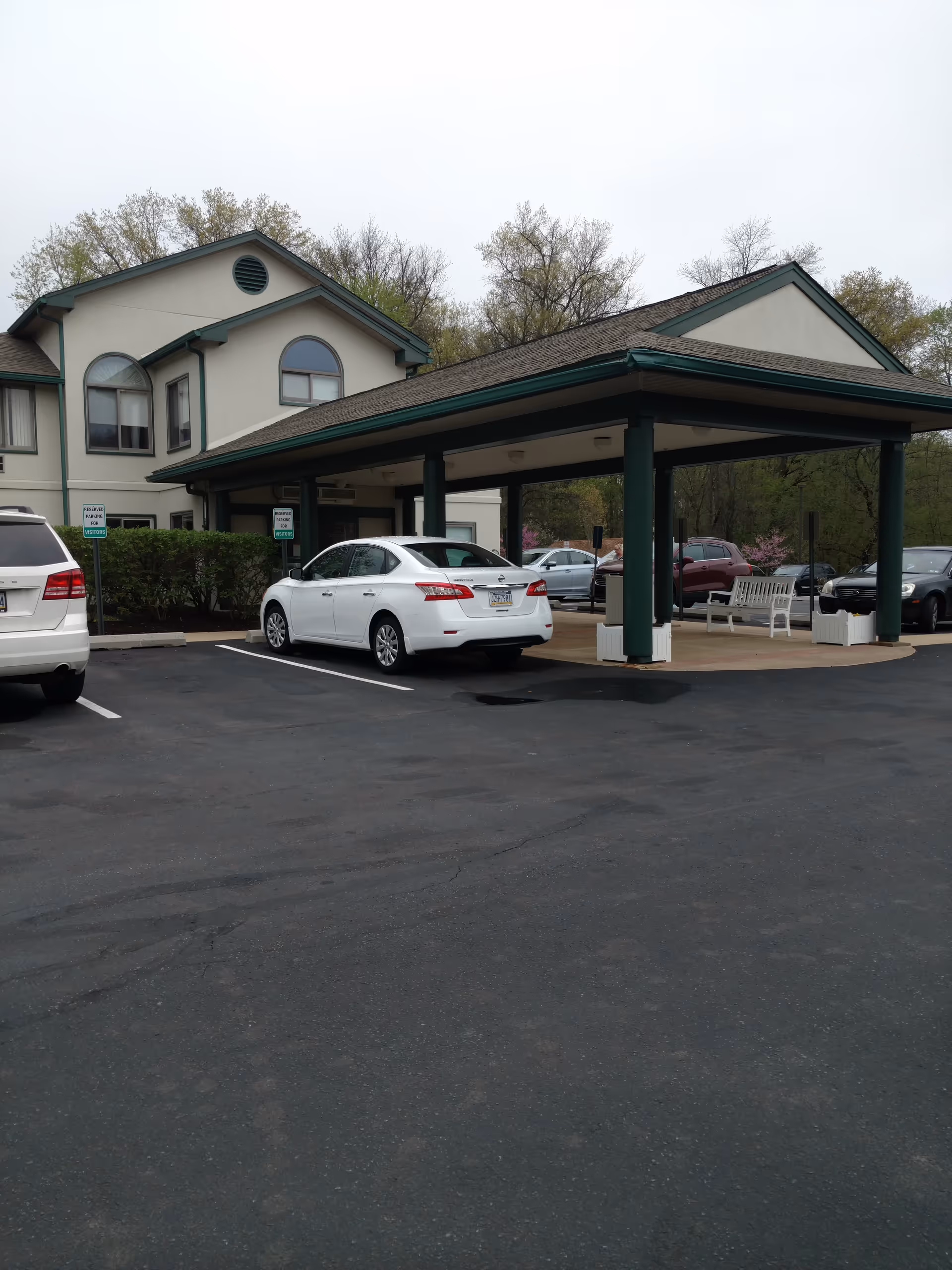 Exterior view of Naamans Creek Country Manor entrance with a covered driveway and parked cars.