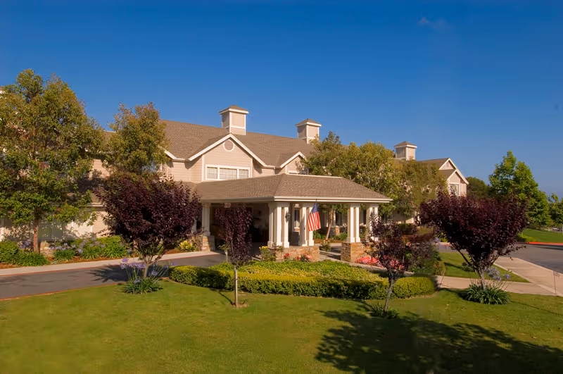 A senior living facility with manicured grounds and an American flag at the front entrance.