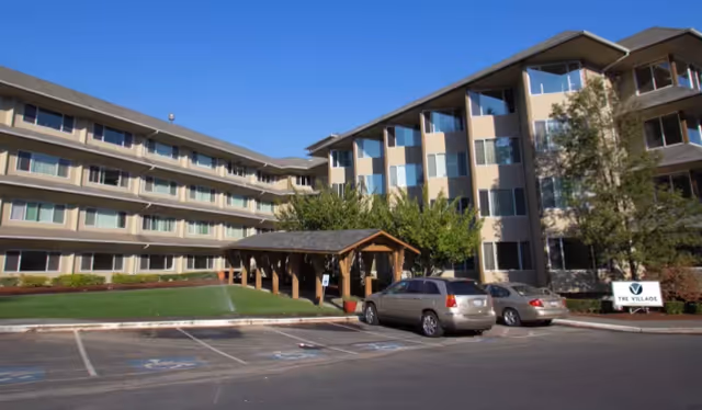 Exterior view of The Village Senior Living with parked cars and a covered entrance.