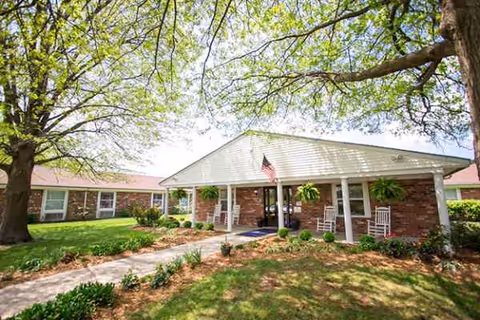 Exterior view of a senior living facility entrance with a covered porch and landscaping.