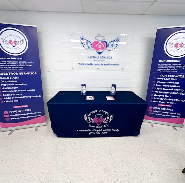 An indoor display booth with banners and a blue table for Loving Angels Home Care LLC.