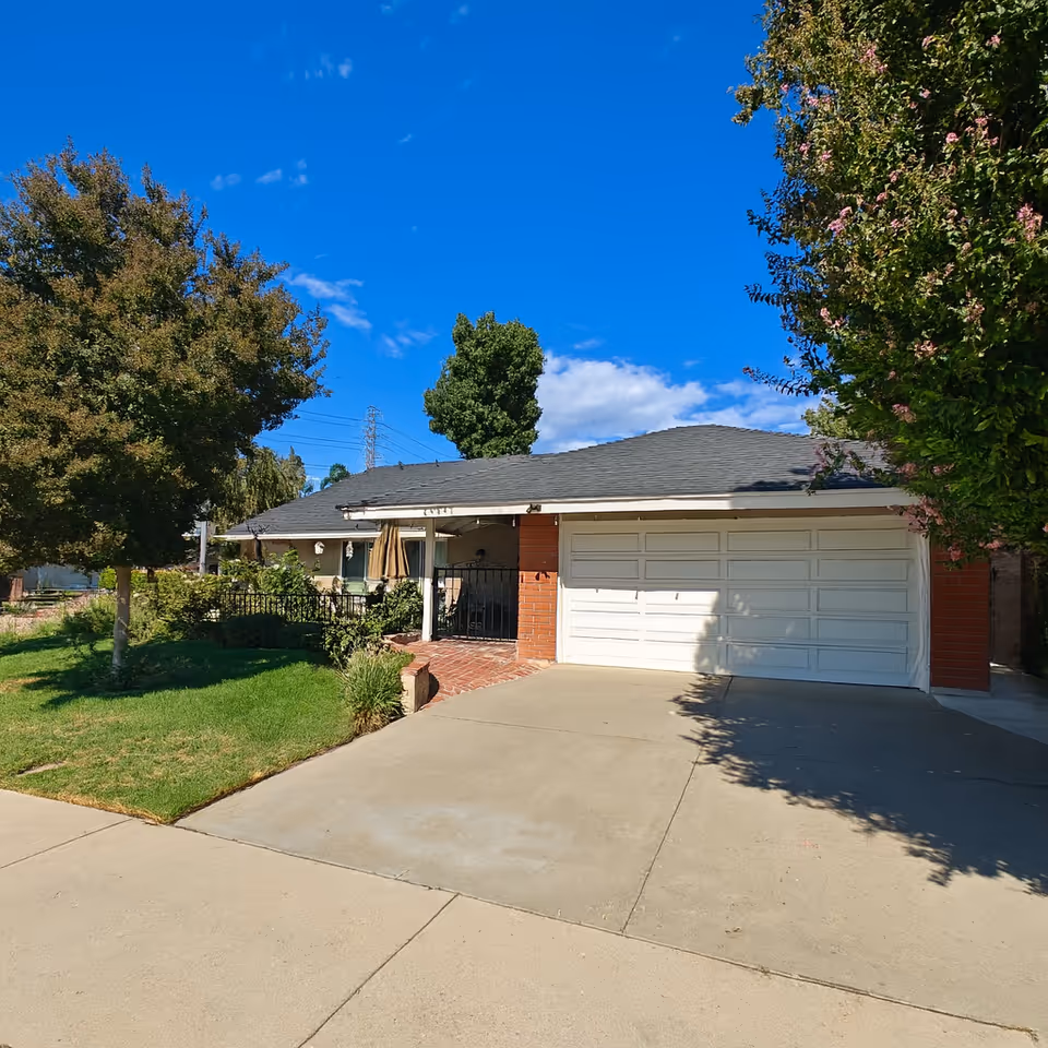 A single-story house with a two-car garage, front yard, and trees.