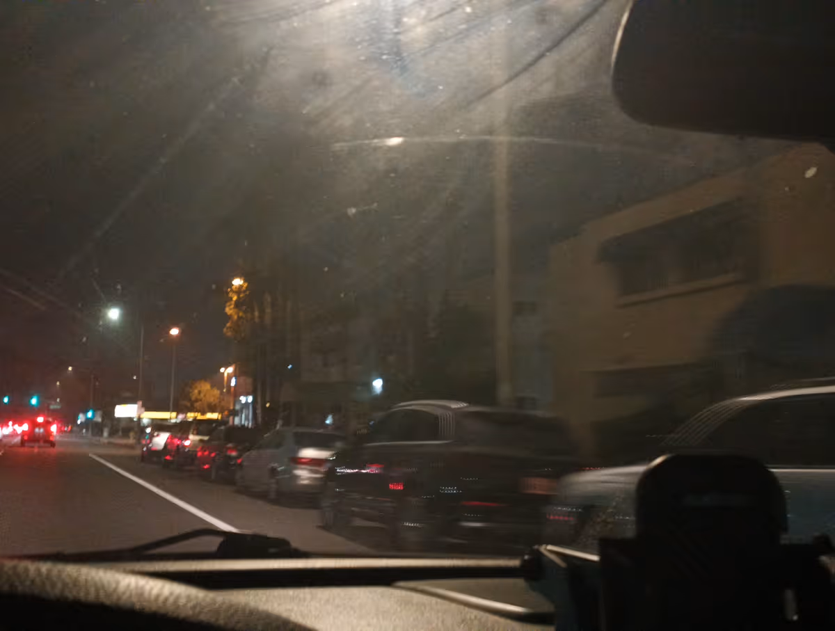 Nighttime street view from inside a car, showing parked cars and a building along the road.