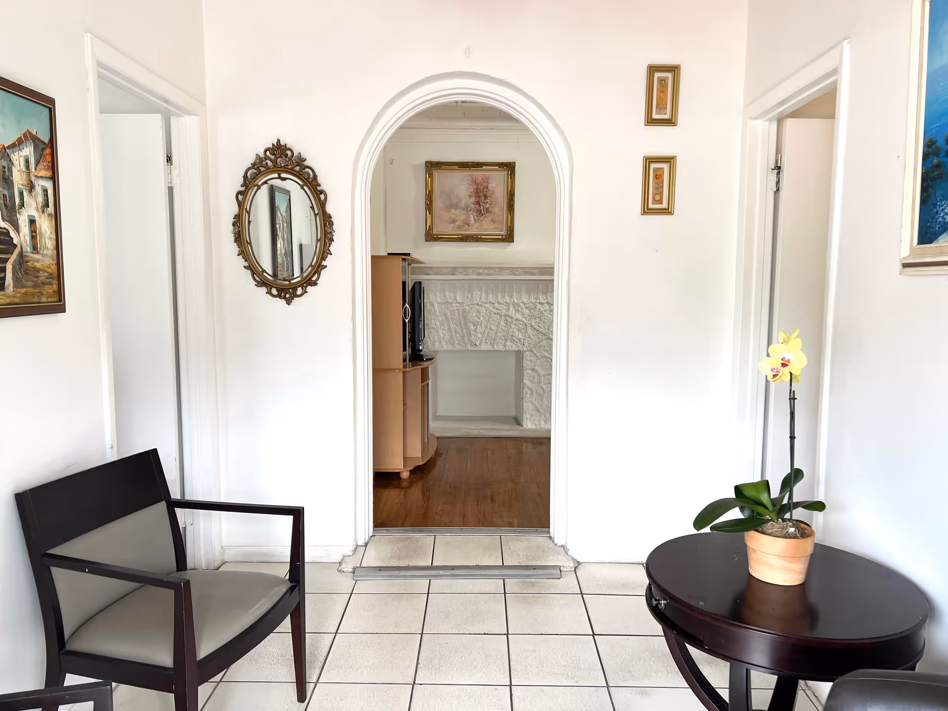 Bright waiting area with white walls, arched doorway, wooden chairs, and a round table with orchid.