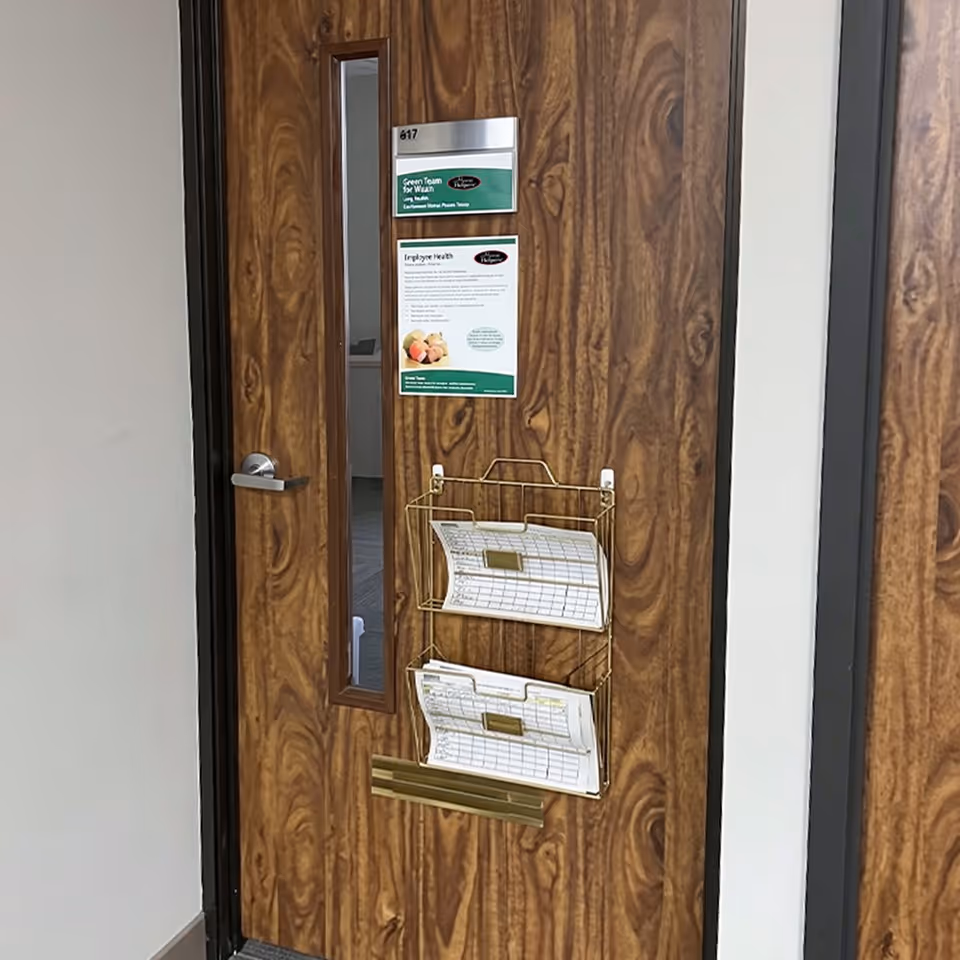 Woodgrain interior door with wall-mounted brochure rack and posted notices in a hallway.