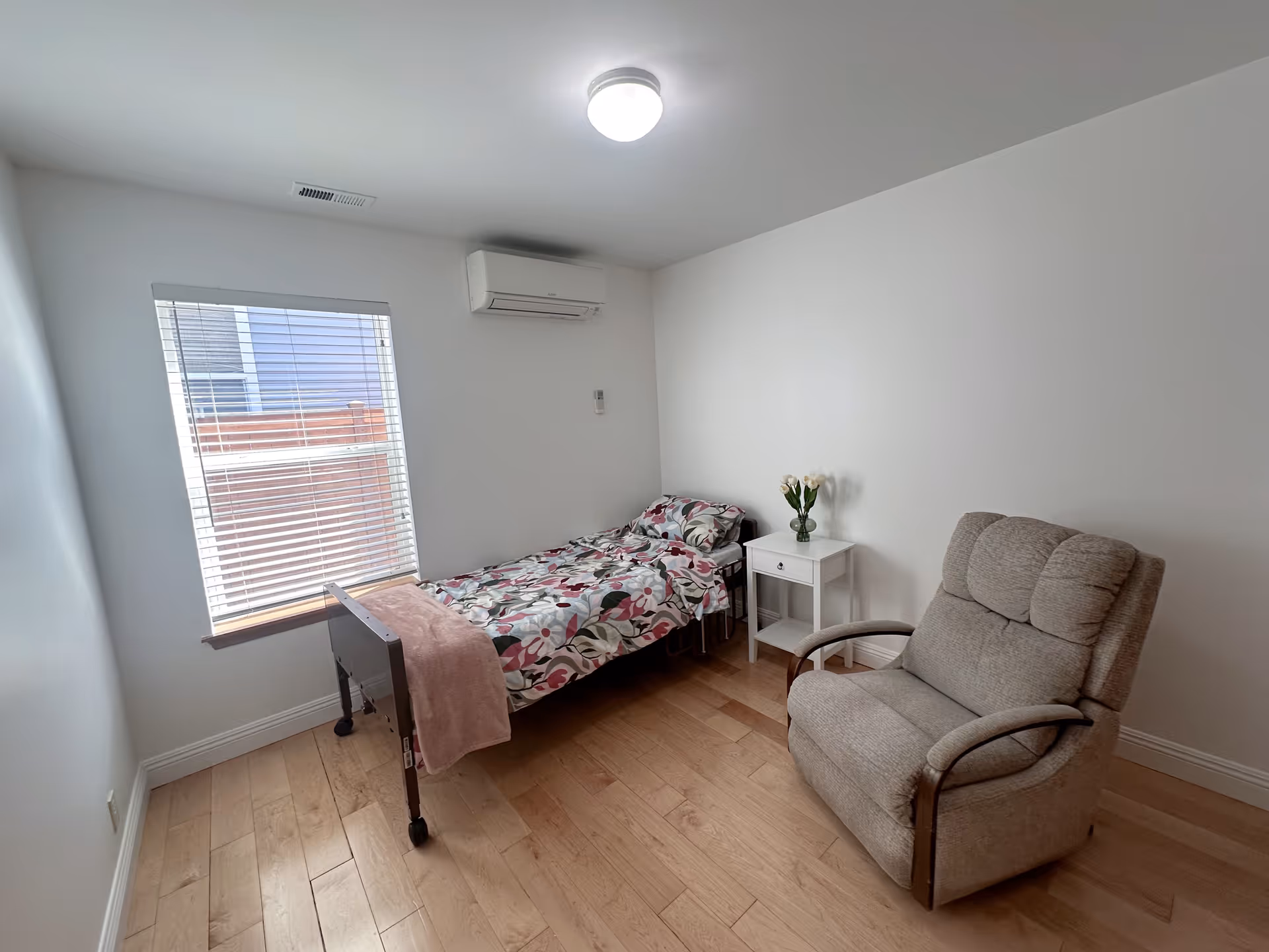 Small bedroom with a single bed, floral bedding, white nightstand, and beige armchair.