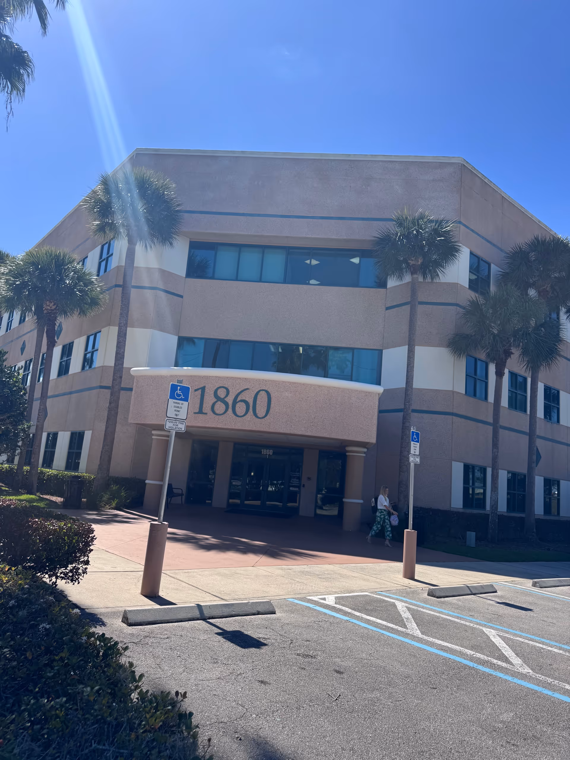 Front view of a tan building with blue-tinted windows, palm trees, and a labeled entrance 1860.