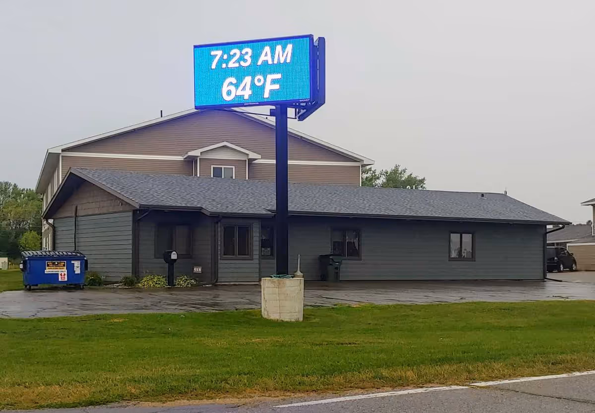 Exterior view of a gray facility building with a large blue digital sign in front.