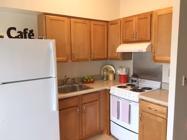 Small kitchen with wooden cabinets, a white refrigerator and stove, and a sink on the countertop.