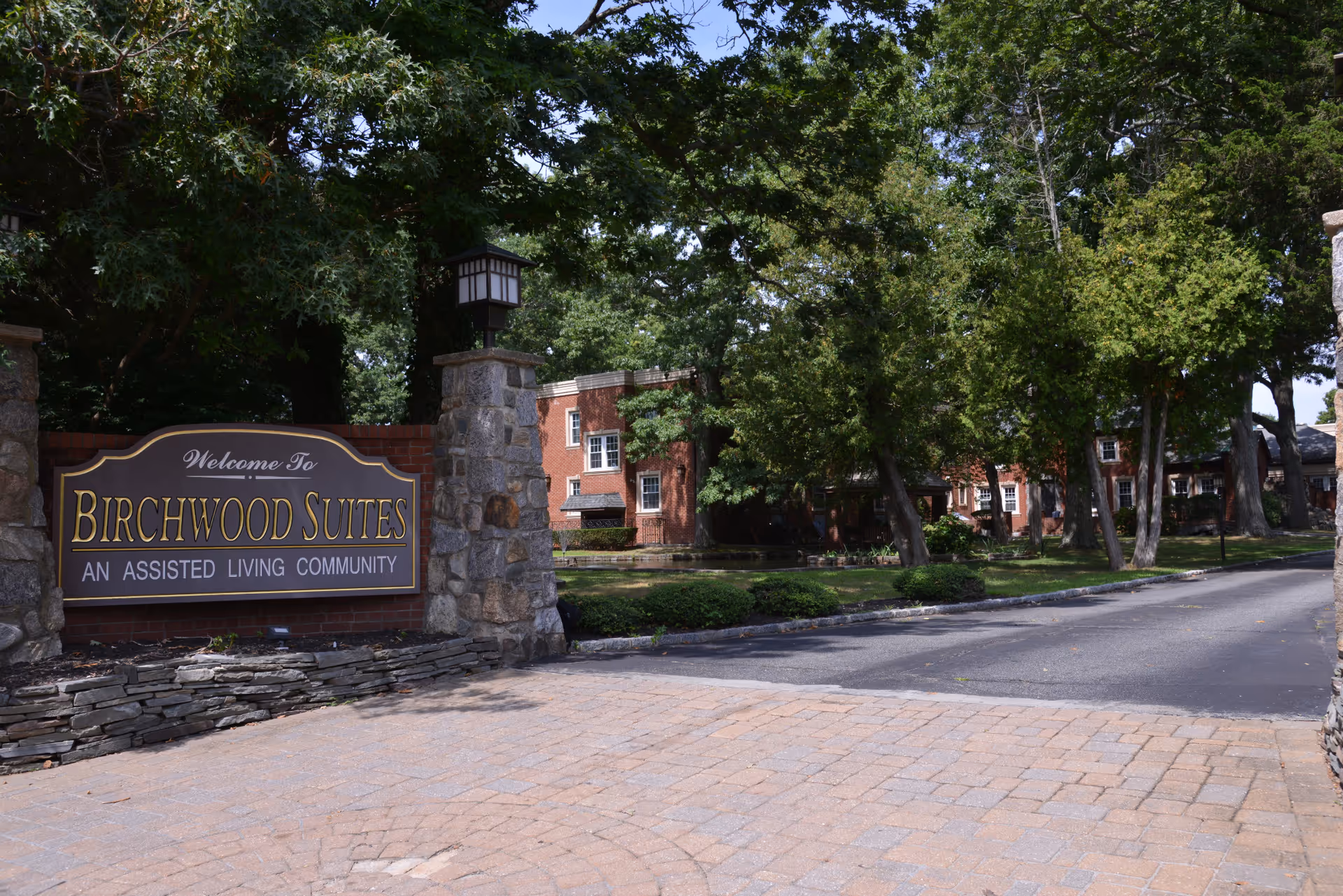 Entrance sign reads Birchwood Suites, an assisted living community, with brick building and trees.