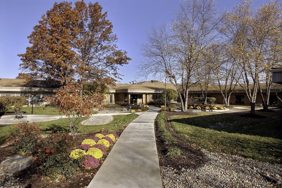 A curved concrete walkway leads to a single-story Greenfield Healthcare Center surrounded by landscaped grounds.