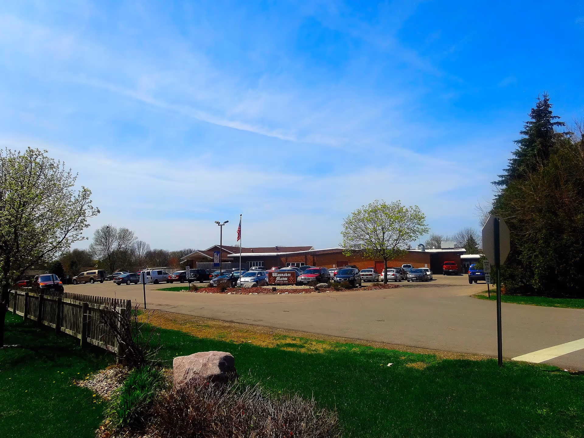 Exterior view of Waunakee Manor with parking lot, trees, and blue sky.