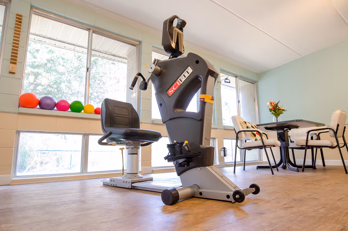 Rehabilitation exercise room with a stationary bike, colorful balls, and a dining table.