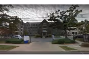 Front exterior view of Inglis House senior living facility with entrance, trees, and parked cars.