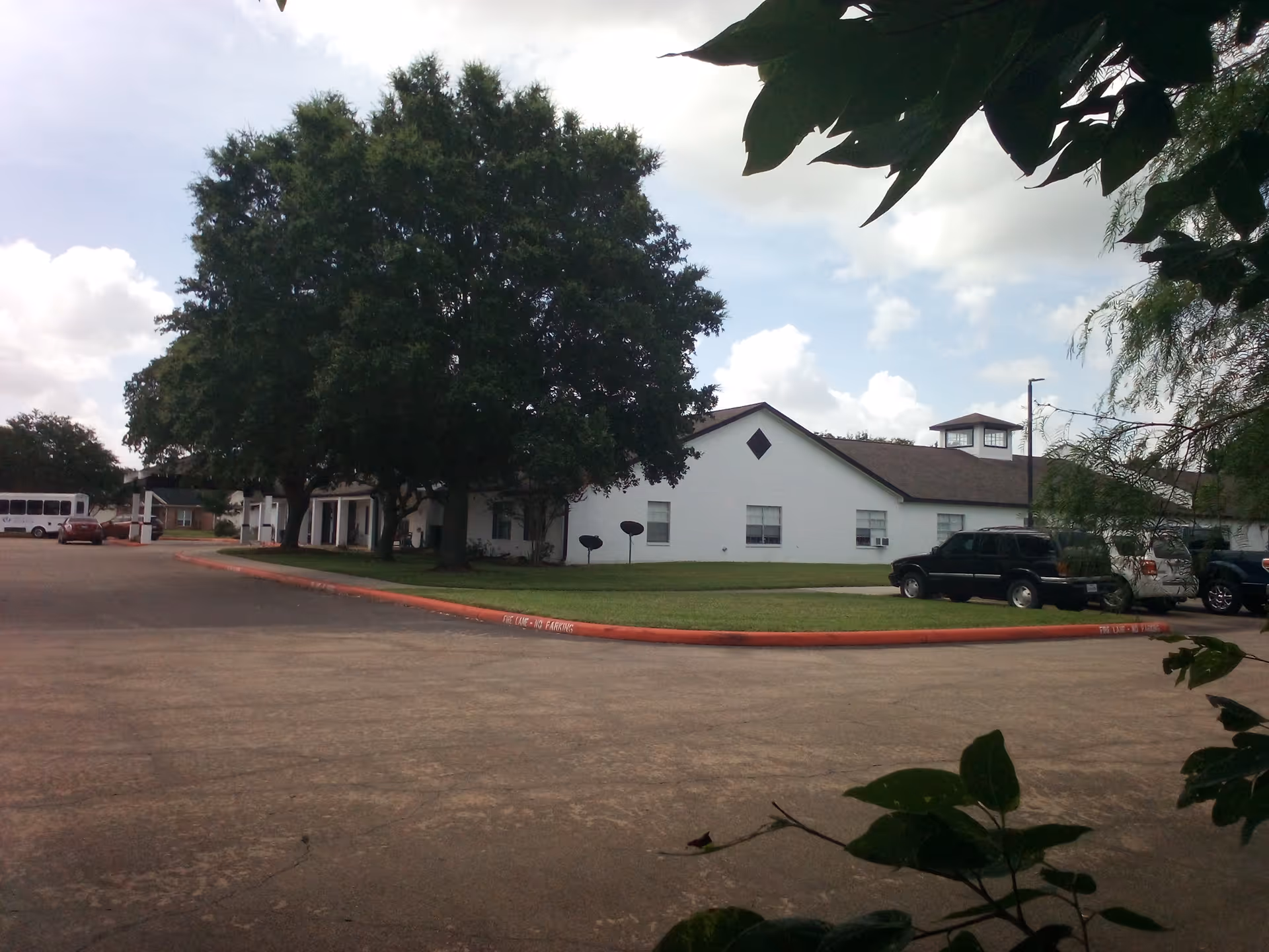 White, single-story senior living facility with trees and a parking lot.