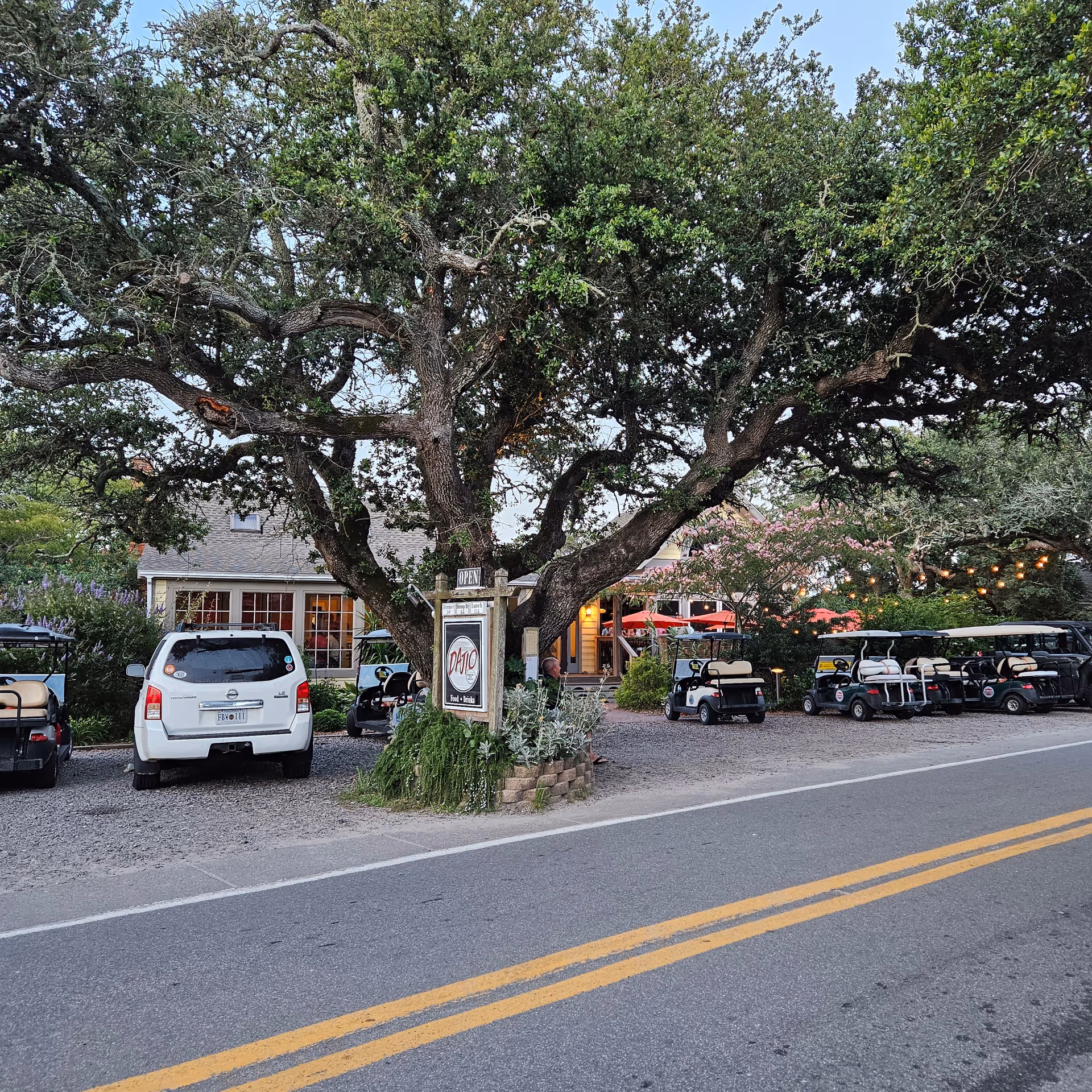 Shaded front area of a building with golf carts and a sign.